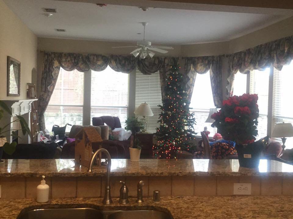 A cozy kitchen and living room setup with holiday decorations, including a Christmas tree near large windows with curtains.