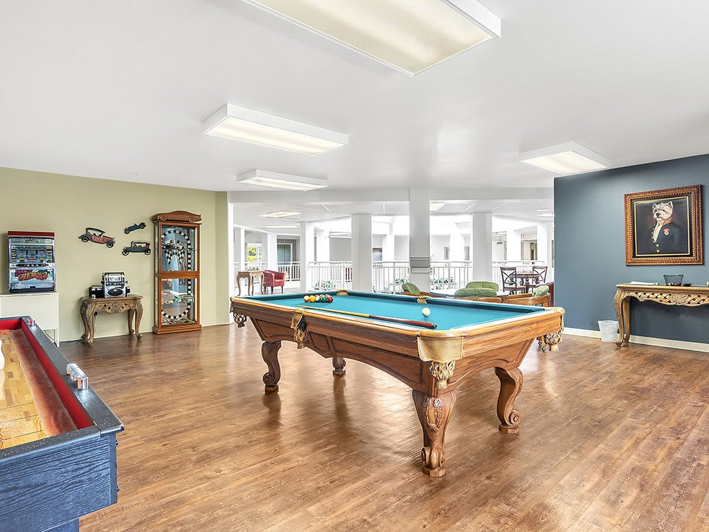 A spacious game room featuring a pool table with wooden flooring and modern decor.