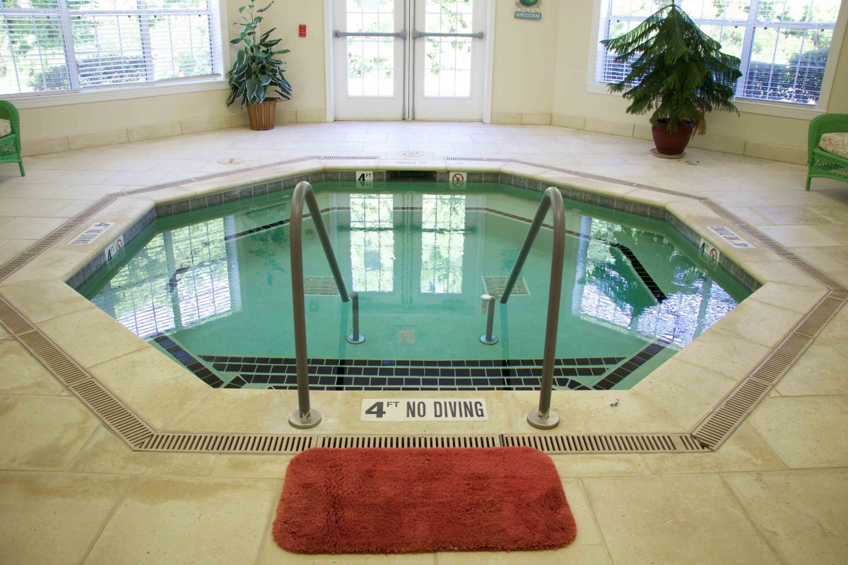 An indoor hot tub featuring steps for entry, with 'No Diving' warning and surrounded by potted plants.