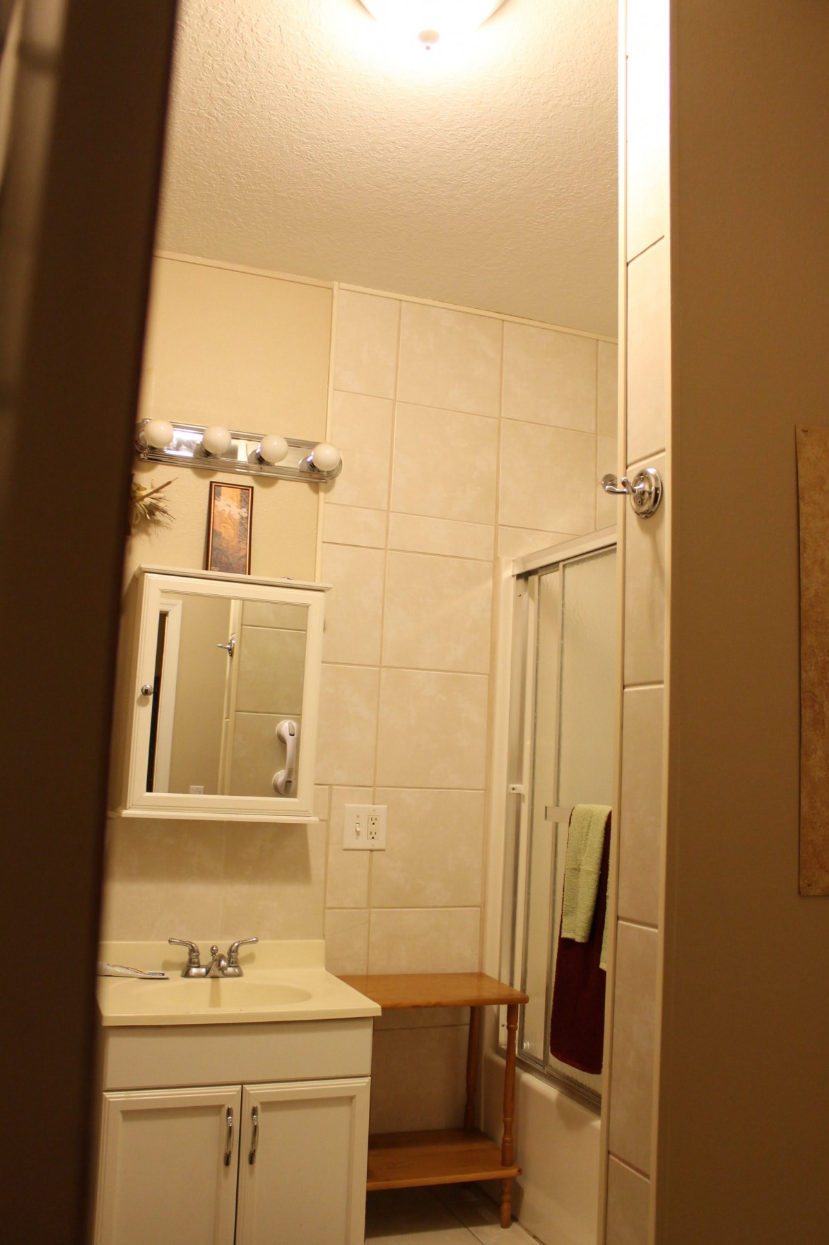 A view of a bathroom featuring a sink, mirror, and shower area with towels hanging.