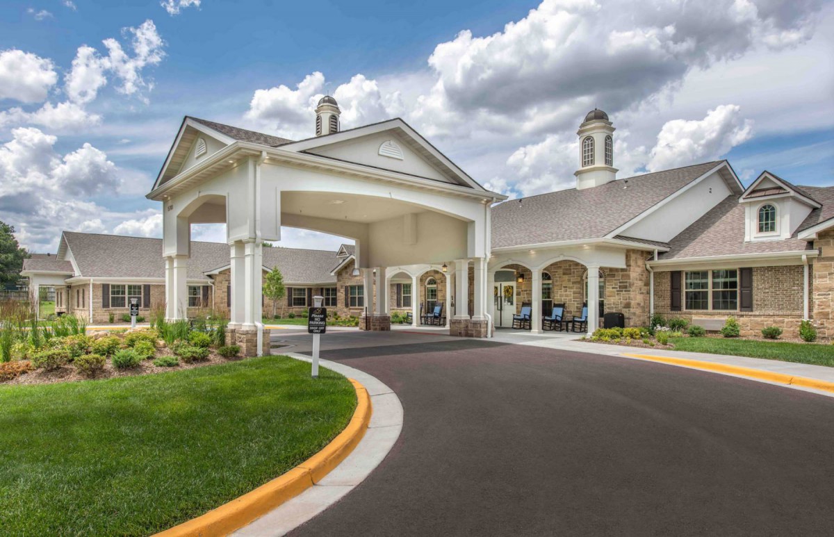 Elegant building entrance with a covered driveway and landscaped surroundings on a cloudy day.