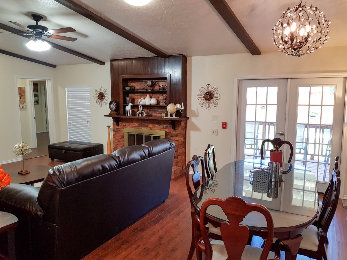 A cozy living and dining area featuring a leather sofa, fireplace, and a chandelier, with french doors leading outside.