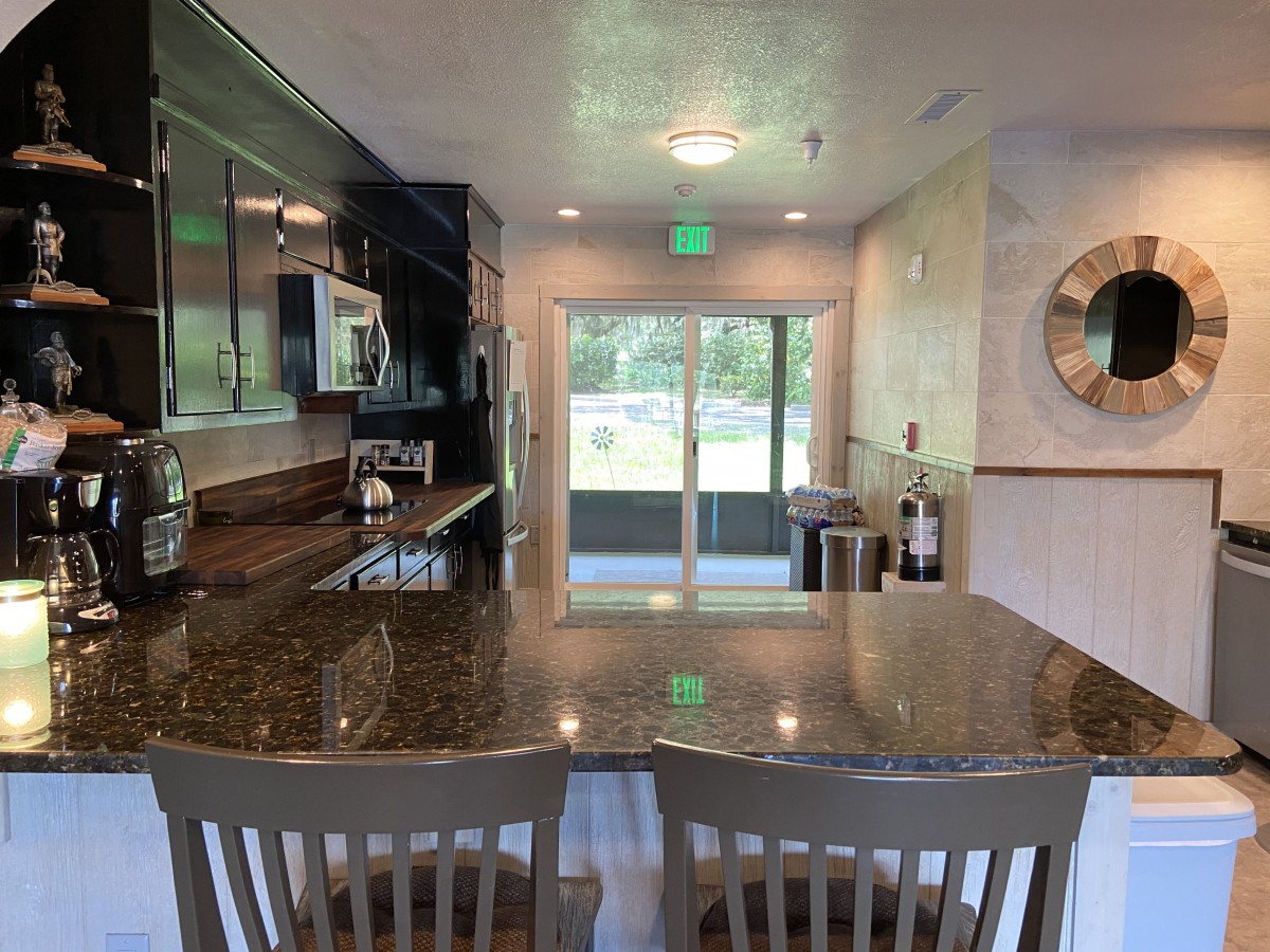 A modern kitchen interior featuring a large countertop and bar stools with a clear view of the outside through sliding doors.