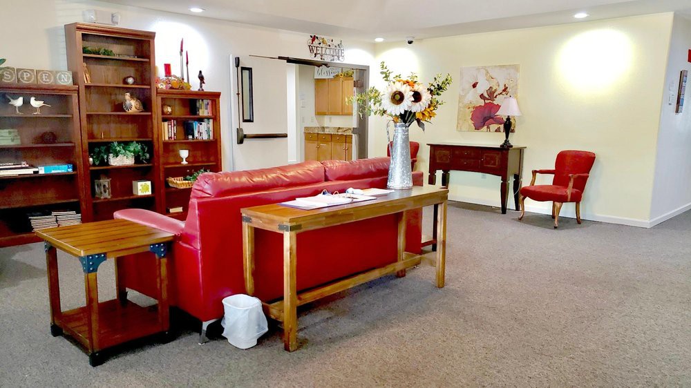 A cozy living room with a red couch, wooden furniture, decorative flowers, and artwork on the walls.