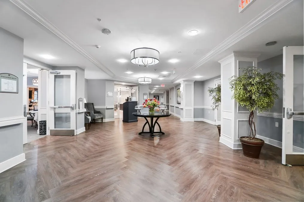 A modern and elegant lobby with stylish flooring, centered around a decorative table with flowers and illuminated by chandeliers.