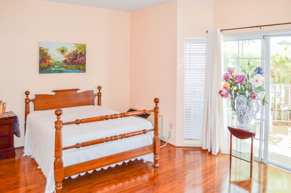 A cozy bedroom featuring a wooden bed, hardwood flooring, and floral accents.