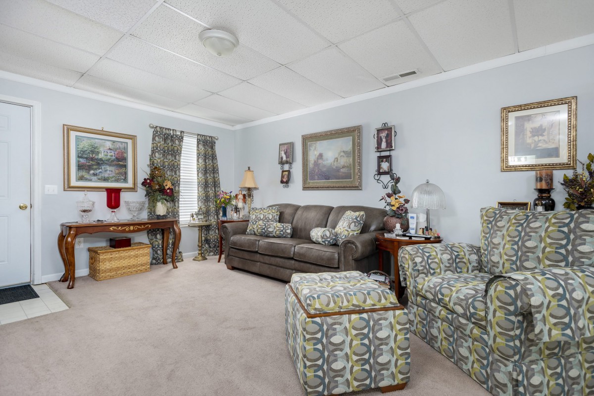 A cozy living room with patterned furniture, artwork on the walls, and a carpeted floor.