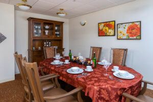 A dining room with a red tablecloth set for a meal, featuring a china cabinet and decorative paintings on the wall.