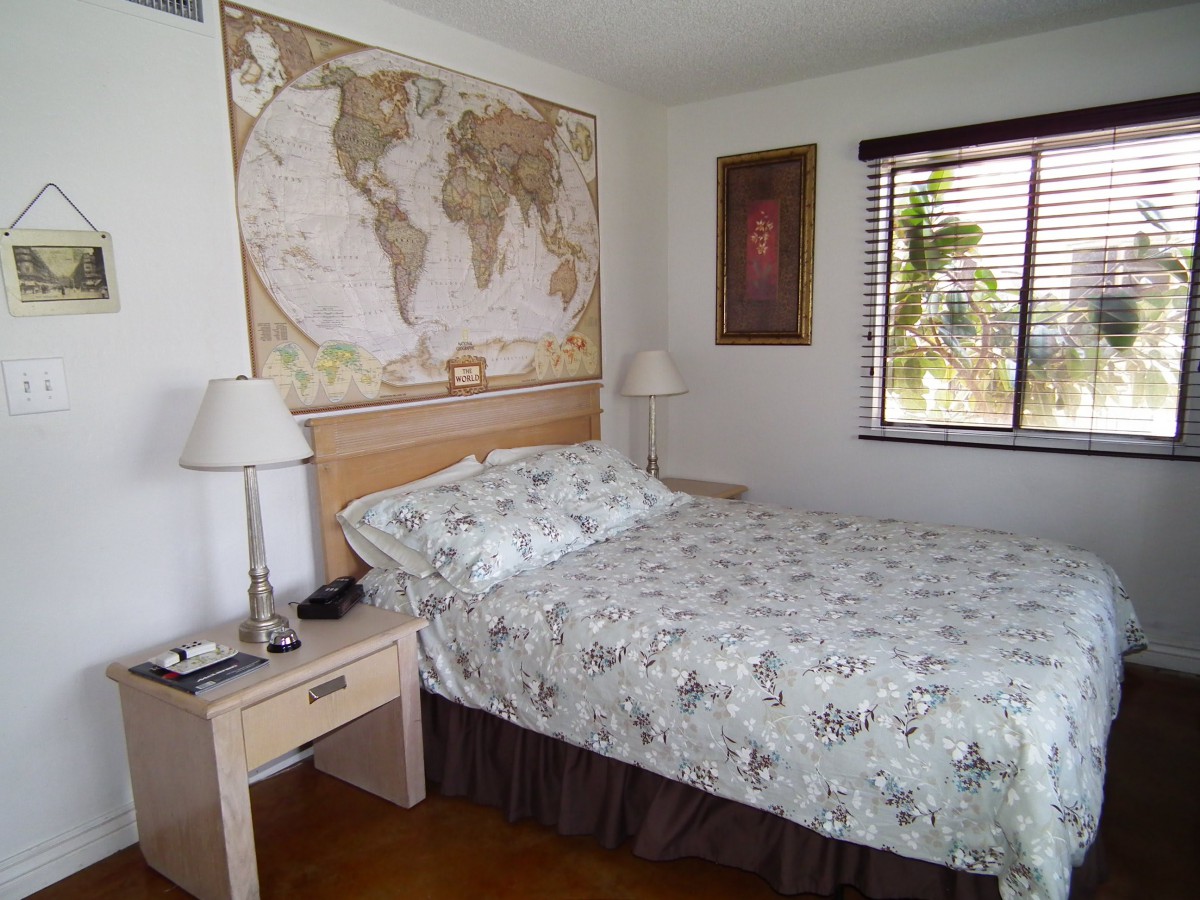 A cozy bedroom with a world map hanging above the bed and natural light coming through the window.