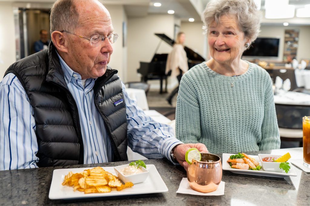 An elderly couple enjoys a meal and conversation in a cozy indoor setting.