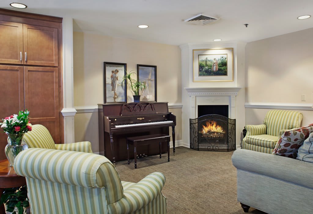 A cozy living room featuring a piano, fireplace, and comfortable armchairs.