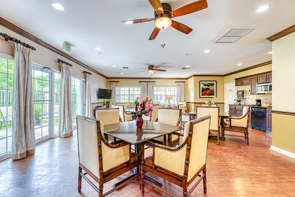 A spacious and elegantly decorated dining room with a central table, surrounded by cushioned chairs and illuminated by ceiling fans, showcasing a cozy and inviting atmosphere.