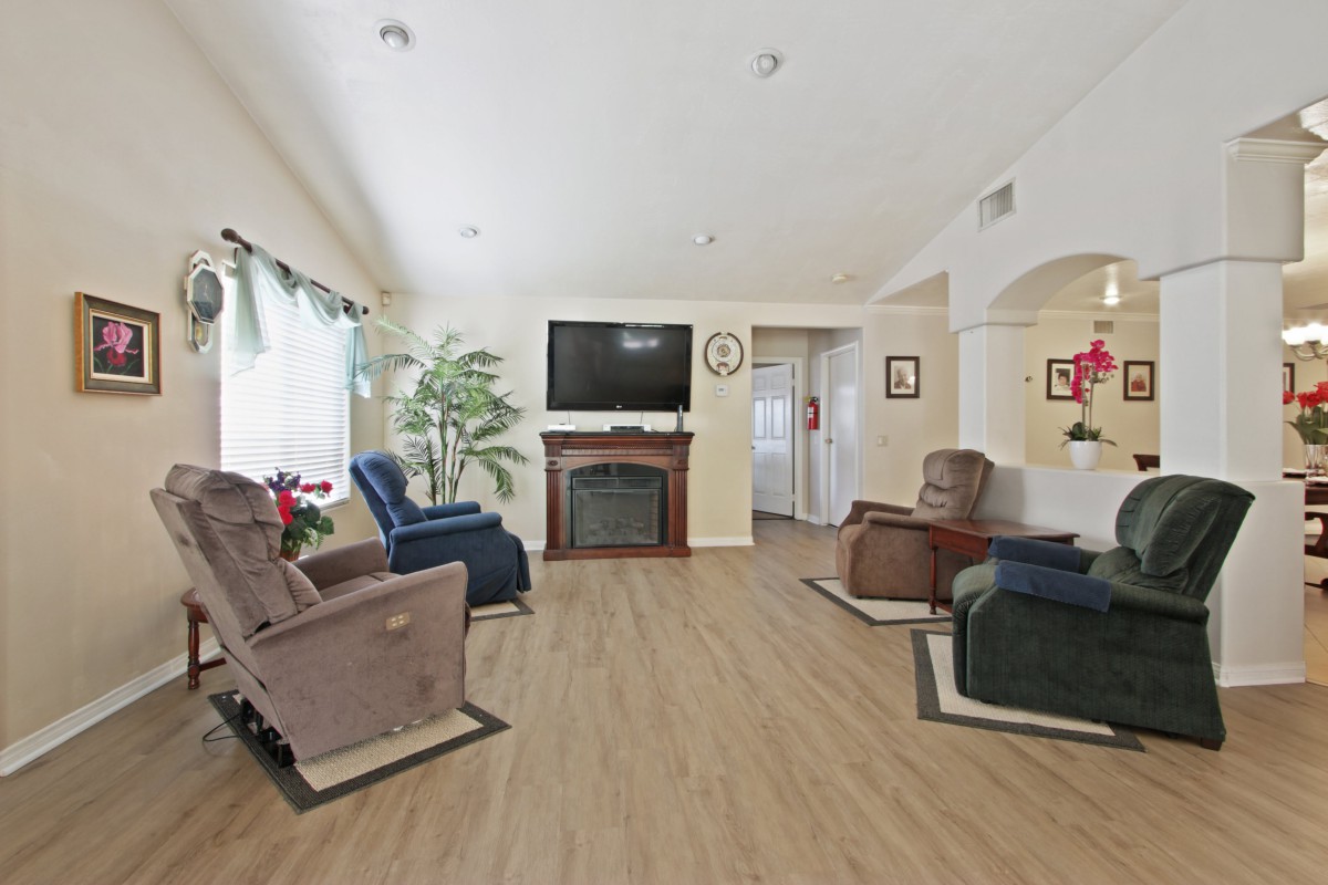 A cozy living room with multiple recliners, a television above a fireplace, and indoor plants enhancing the decor.