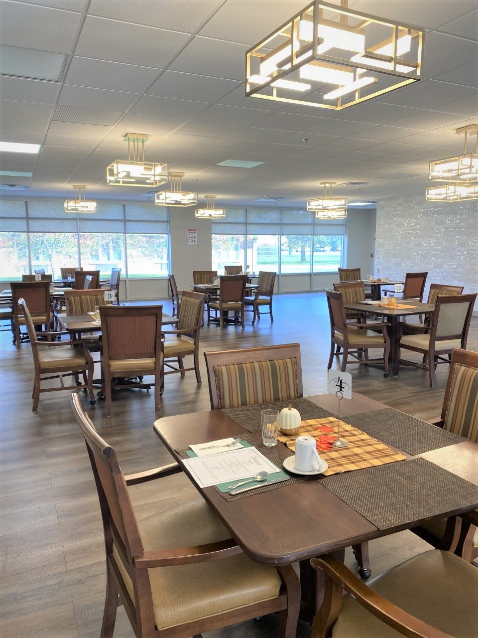 A spacious dining room with multiple tables and chairs, featuring elegant lighting and large windows.