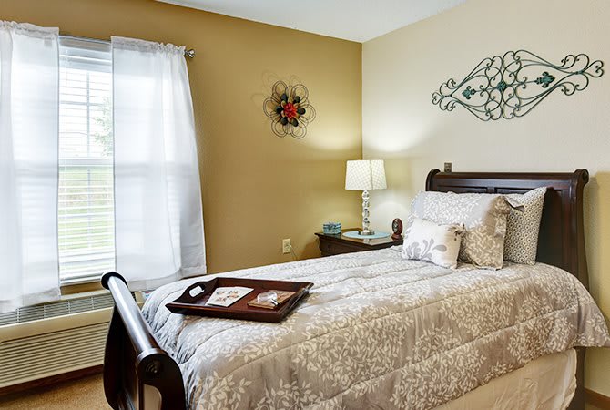 A cozy bedroom with a neatly made bed, soft lighting from a bedside lamp, and decorative wall art.