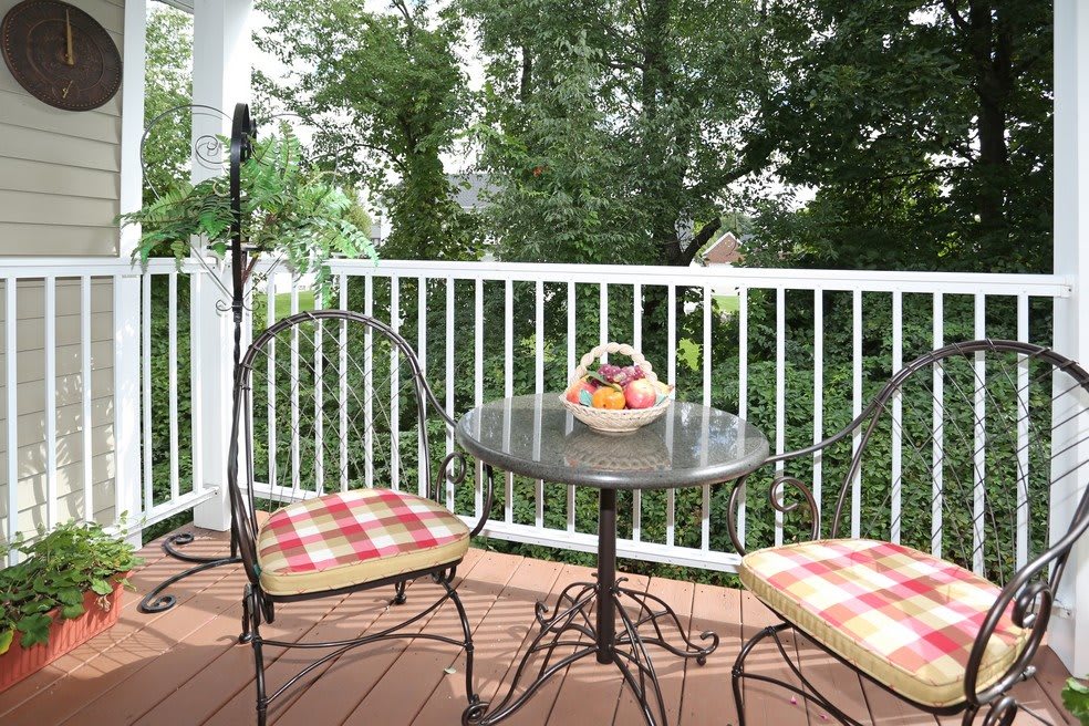 A cozy patio with a small table and two chairs, adorned with a basket of fruit and overlooking lush greenery.