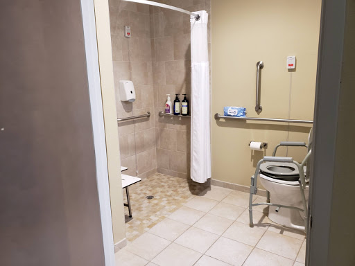 A spacious and accessible bathroom featuring a shower, wheelchair-friendly commode, and safety handrails.