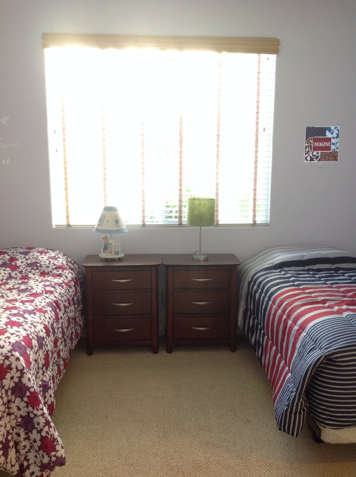 A bright bedroom with two twin beds, a shared dresser, and decorative items by the window.