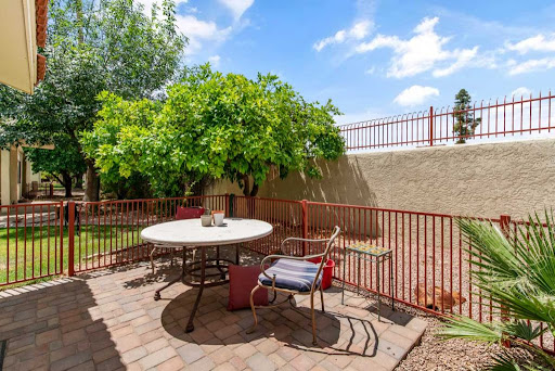 A serene outdoor patio area featuring a round table, chairs, and lush greenery under a clear blue sky.