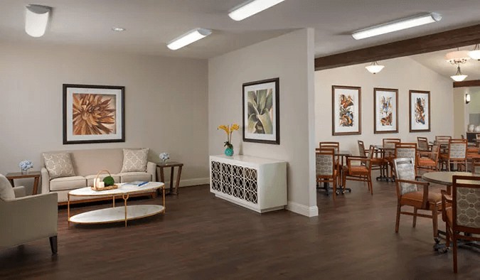 A modern interior featuring a living room with seating and art-adorned walls, leading into a dining area.