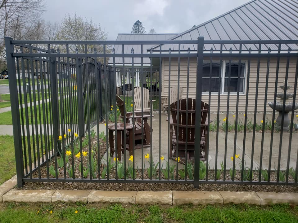 A fenced patio area with wooden chairs and a garden in front of a house.