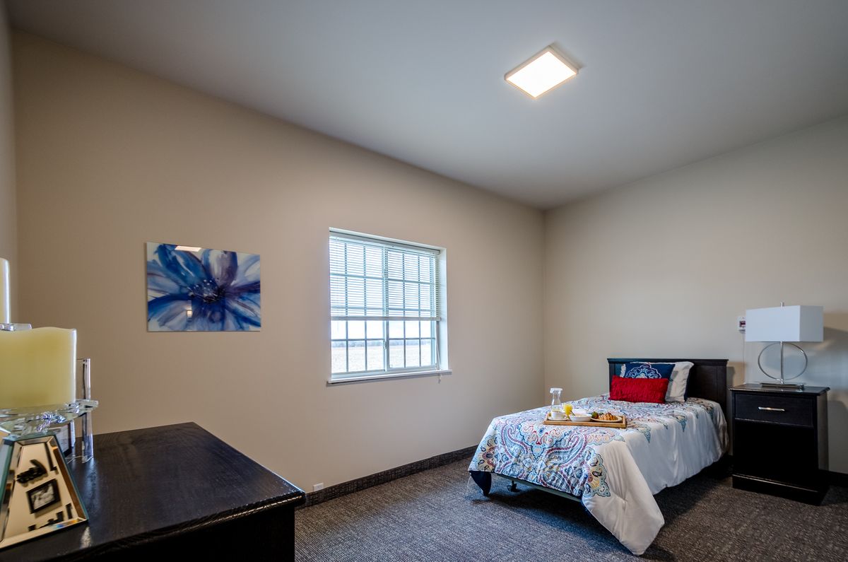A minimalist bedroom with a single bed, painting on the wall, and a window providing natural light.