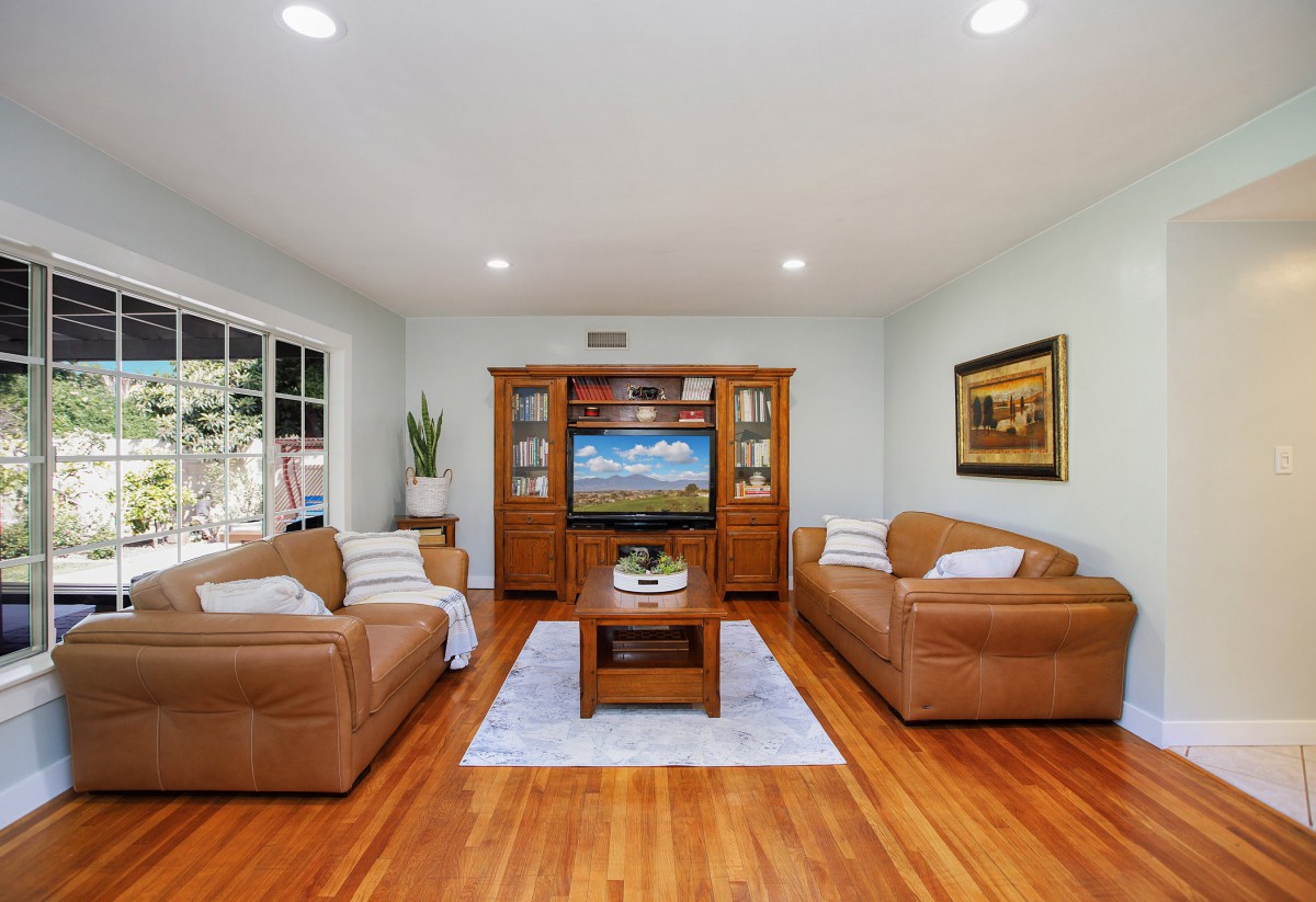 A cozy living room with leather sofas, a wooden coffee table, and a TV entertainment unit on a polished wood floor.