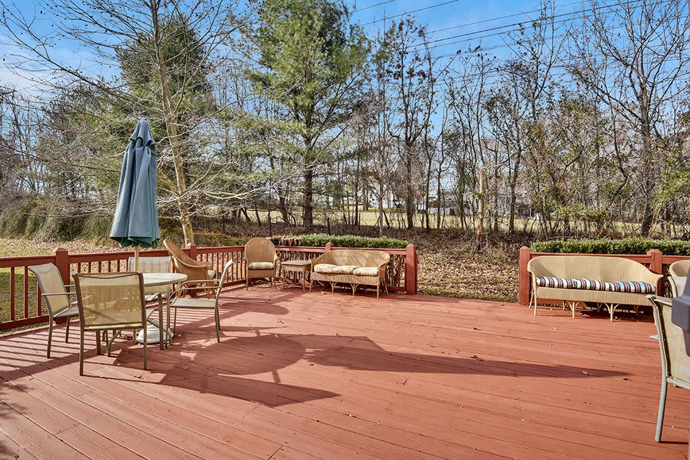 A spacious wooden deck with outdoor furniture and an umbrella, surrounded by trees.