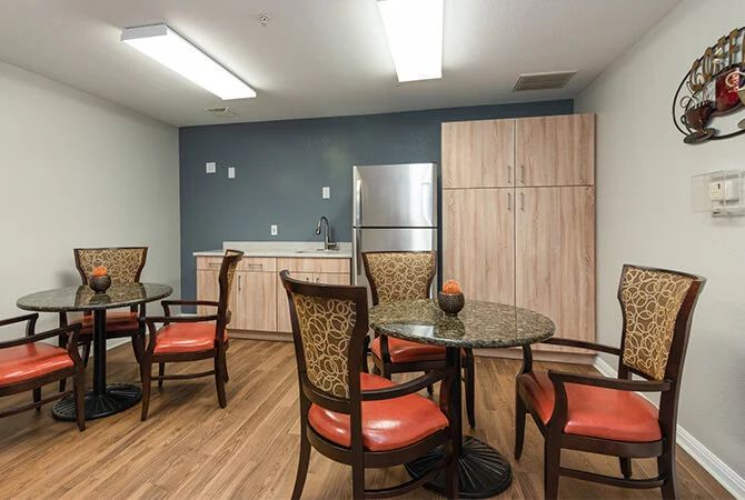 A cozy kitchen area with round tables, cushioned chairs, and modern appliances.