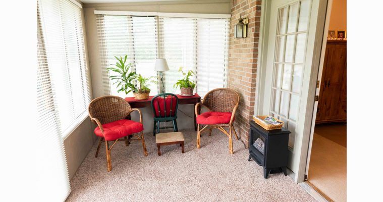 A cozy sunroom with wicker chairs, red cushions, and green plants by a window.