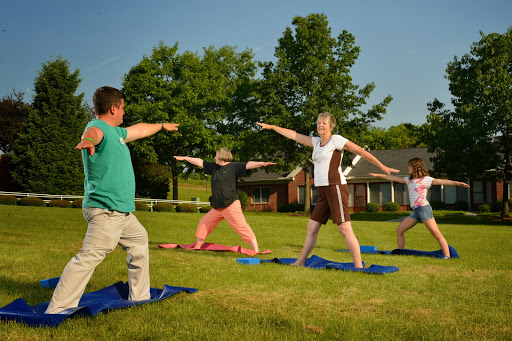 A group of children and adults practicing yoga together in a sunny outdoor setting.