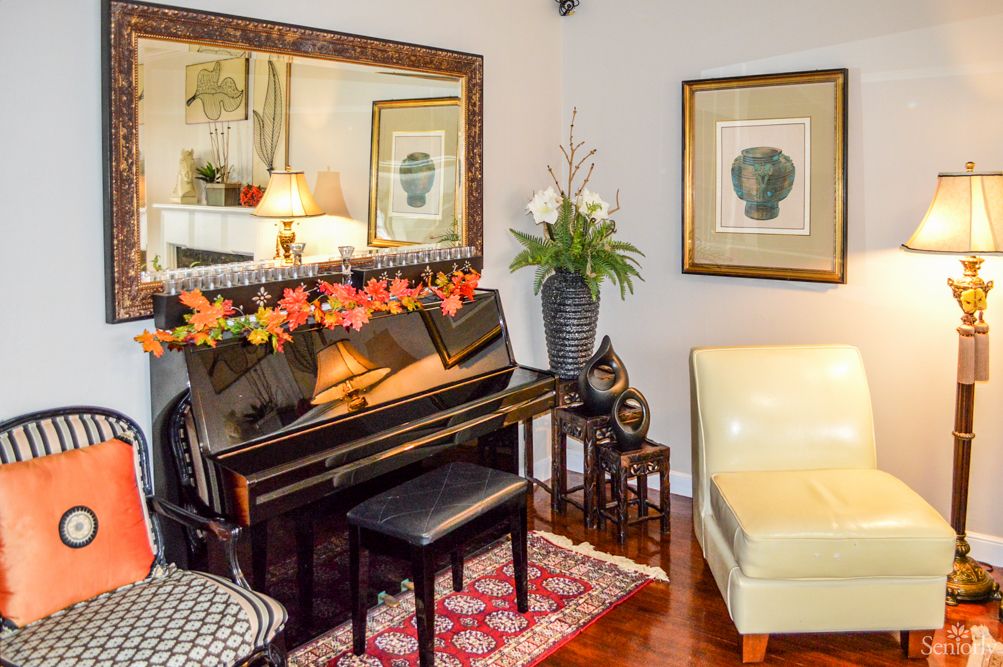 A cozy living room with a decorated piano, mirror, and artwork.