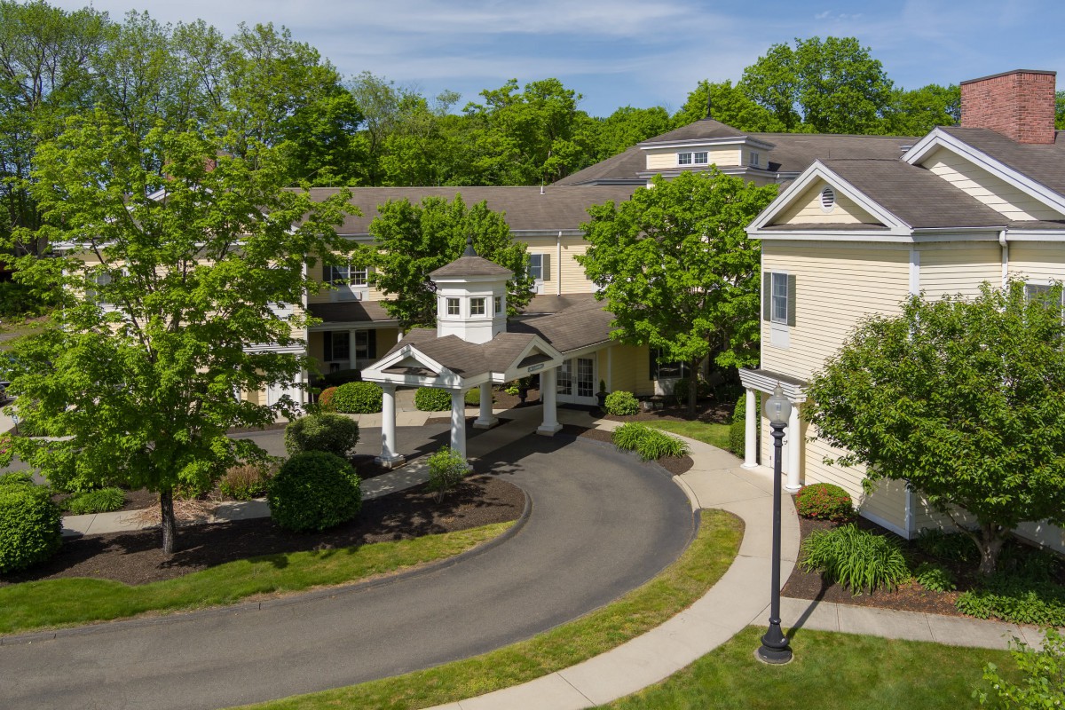 A residential building with a circular driveway surrounded by trees and well-maintained landscaping.