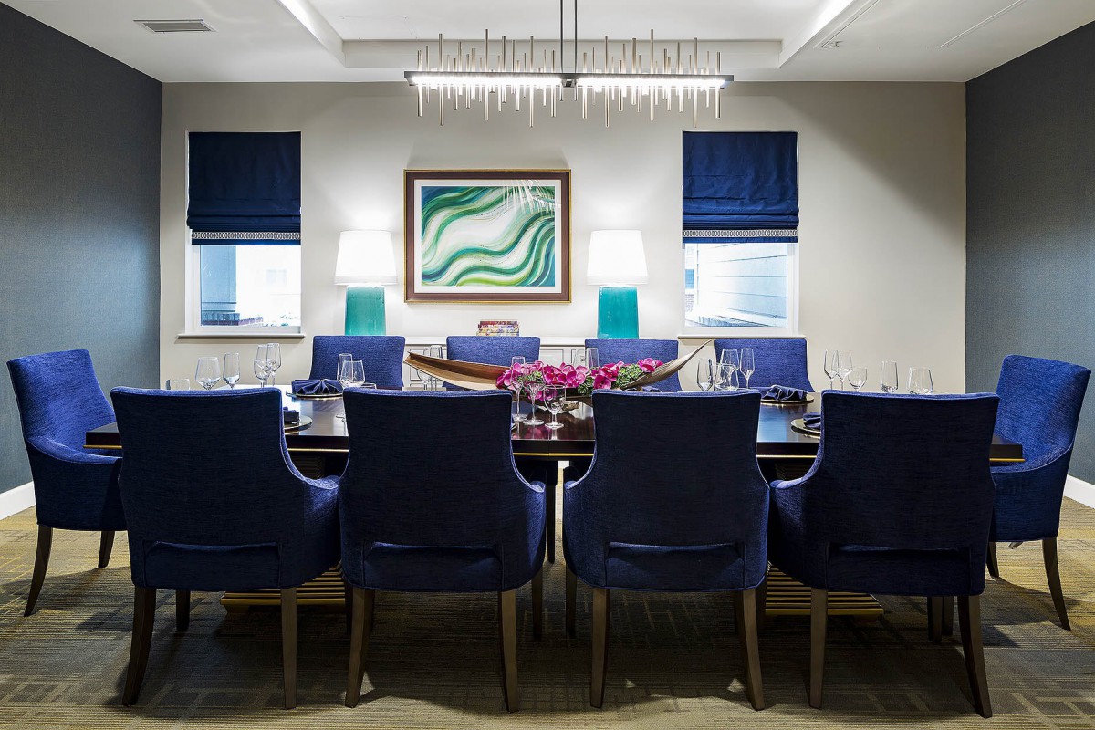 A modern dining room with blue chairs, a stylish chandelier, and contemporary artwork on the wall.