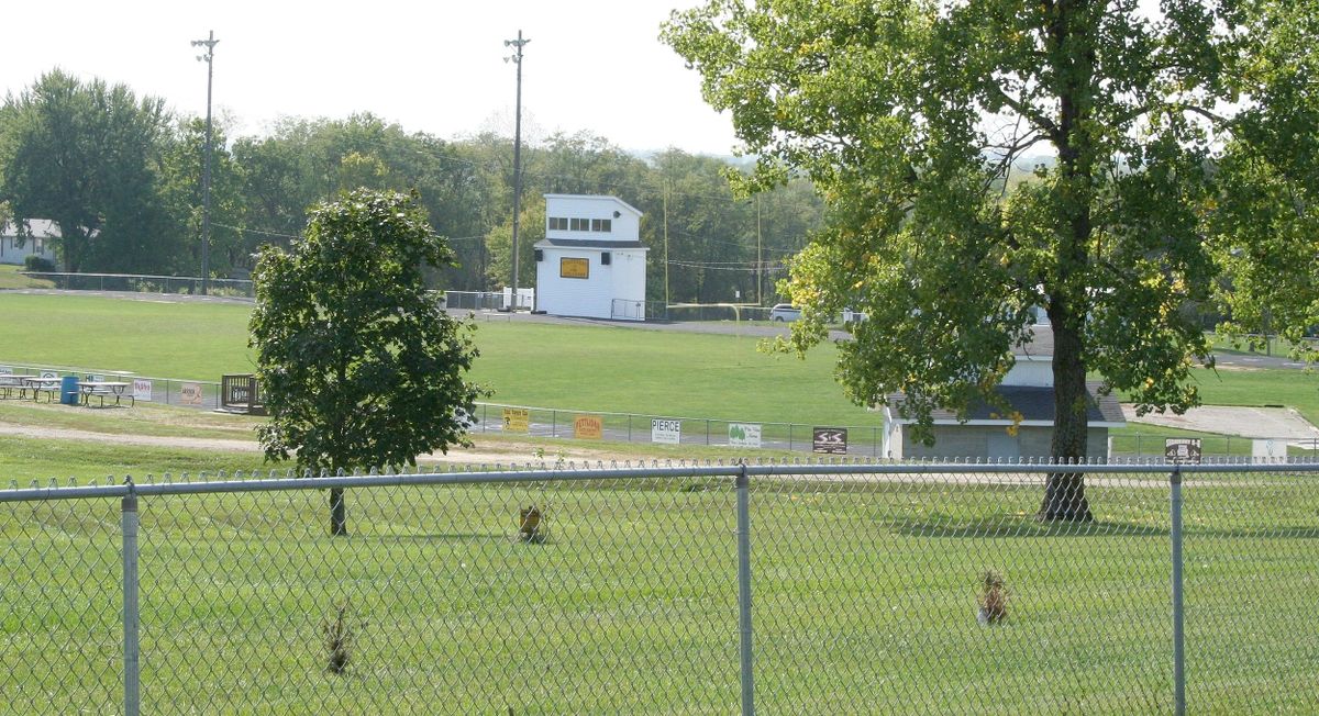 A view of a football field surrounded by trees and a chain-link fence.