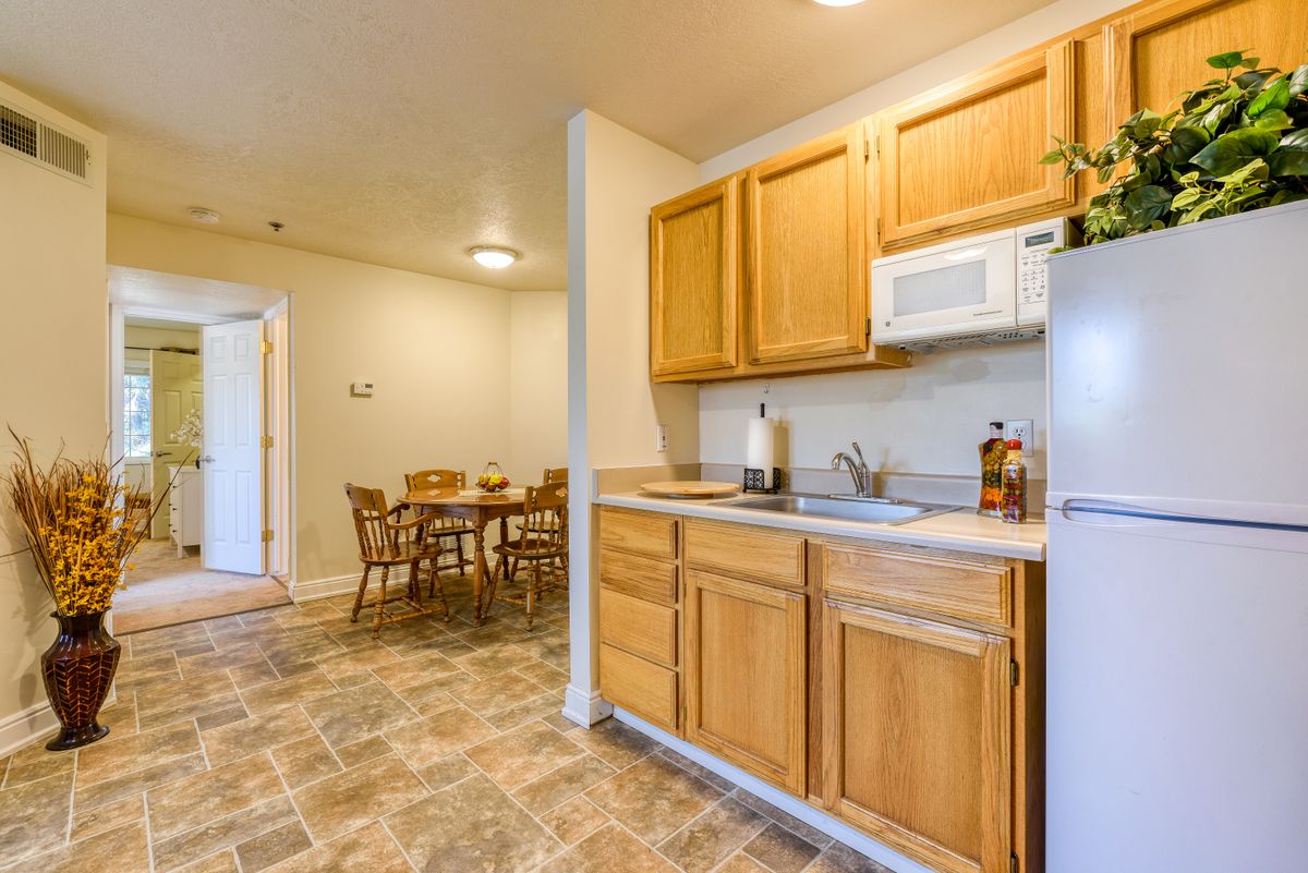 A cozy kitchen and dining area with wooden cabinets, a microwave, refrigerator, and a tiled floor.