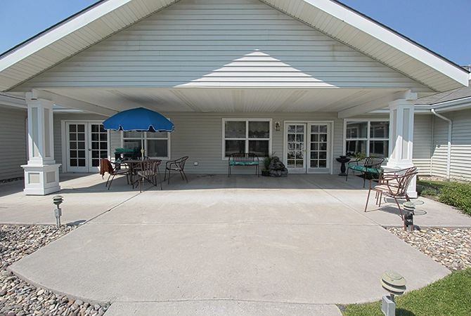 A spacious outdoor patio area with tables, chairs, and a blue umbrella in front of a house.