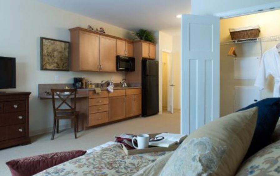 A modern kitchen integrated into a cozy living space, featuring wooden cabinets and essential appliances.