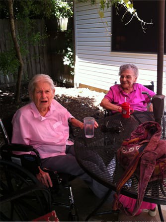 Two elderly women sitting in wheelchairs, enjoying a sunny day outdoors.