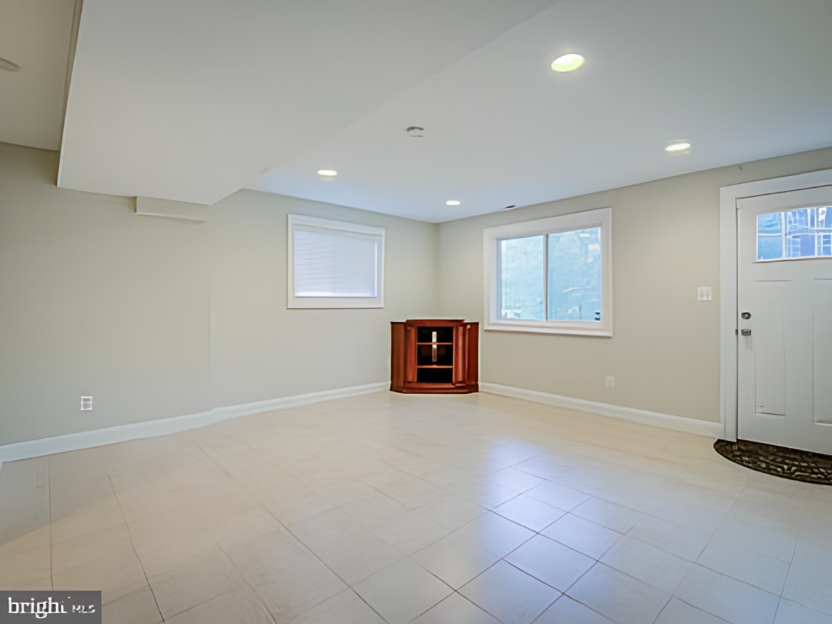 A spacious, empty basement with tiled flooring, recessed lighting, and two windows providing natural light.