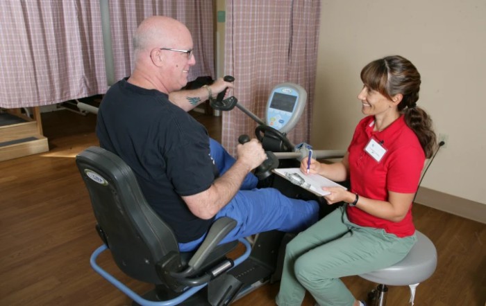 A person undergoing a physical therapy session using fitness equipment with guidance from a healthcare professional.