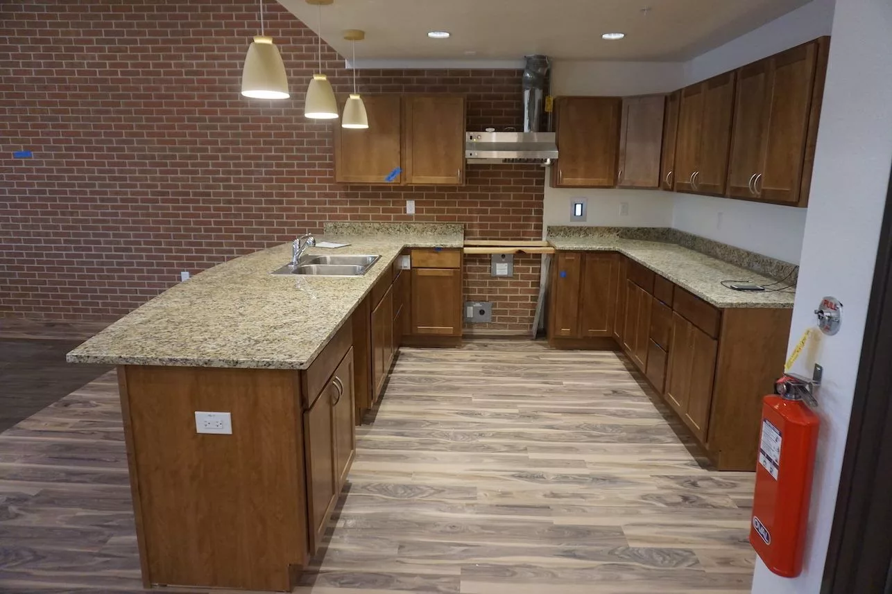 A modern kitchen featuring wooden cabinets, granite countertops, and a brick accent wall with pendant lighting.