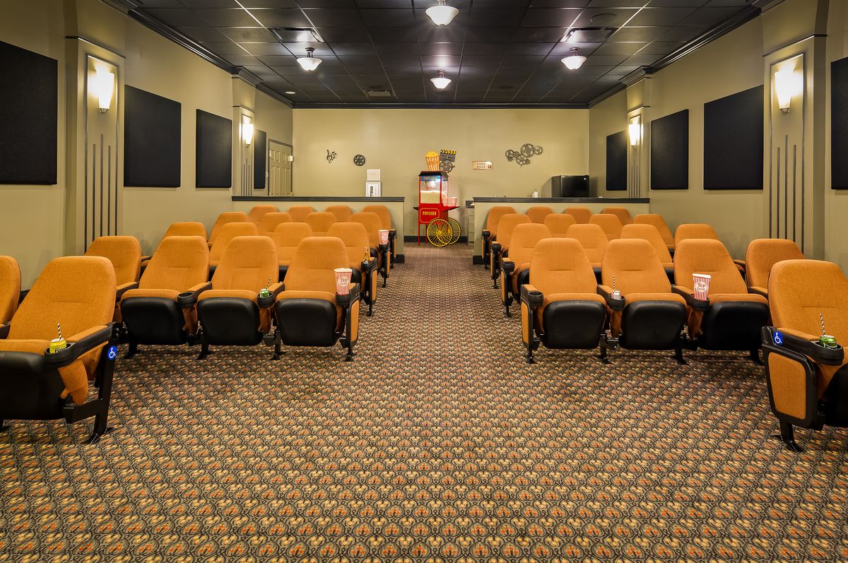 An empty theater with rows of orange seats facing the screen.
