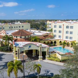 A sunny view of a resort hotel with a swimming pool and palm trees.