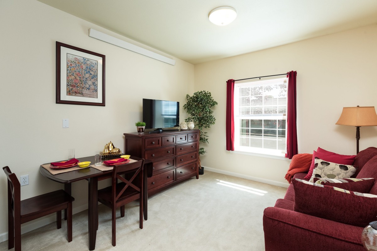 A cozy living room with a red theme, featuring a TV, dining area, and a large window.
