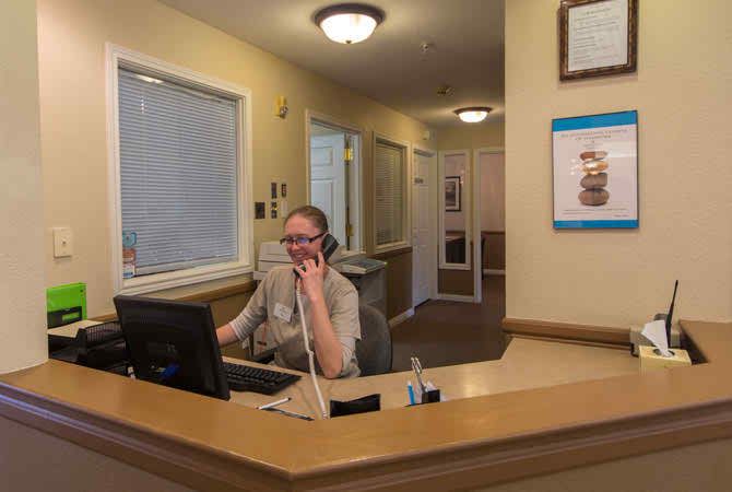 A man sitting at a reception desk talking on the phone in an office setting.