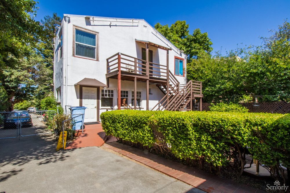 A two-story house with a spacious backyard, featuring a wooden staircase and surrounded by greenery.