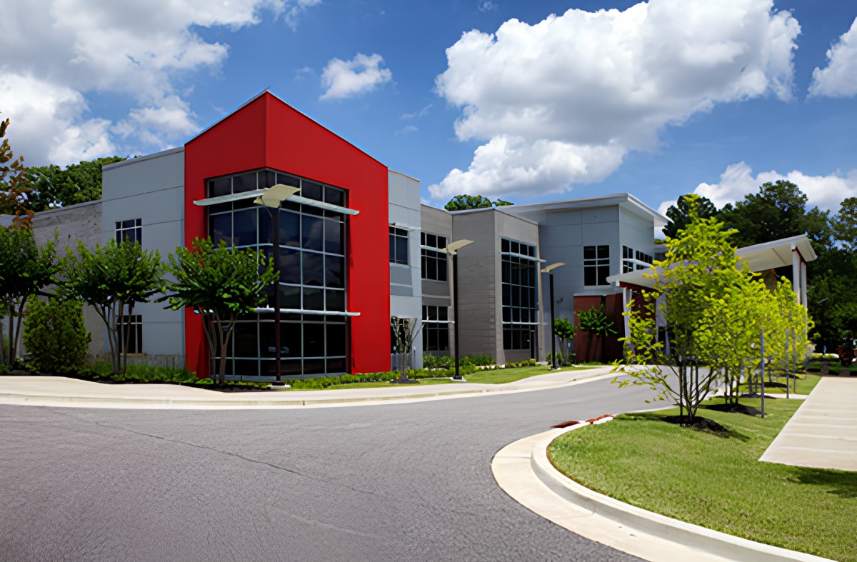 A modern office building with a distinctive red facade, surrounded by trees and set against a partly cloudy sky.