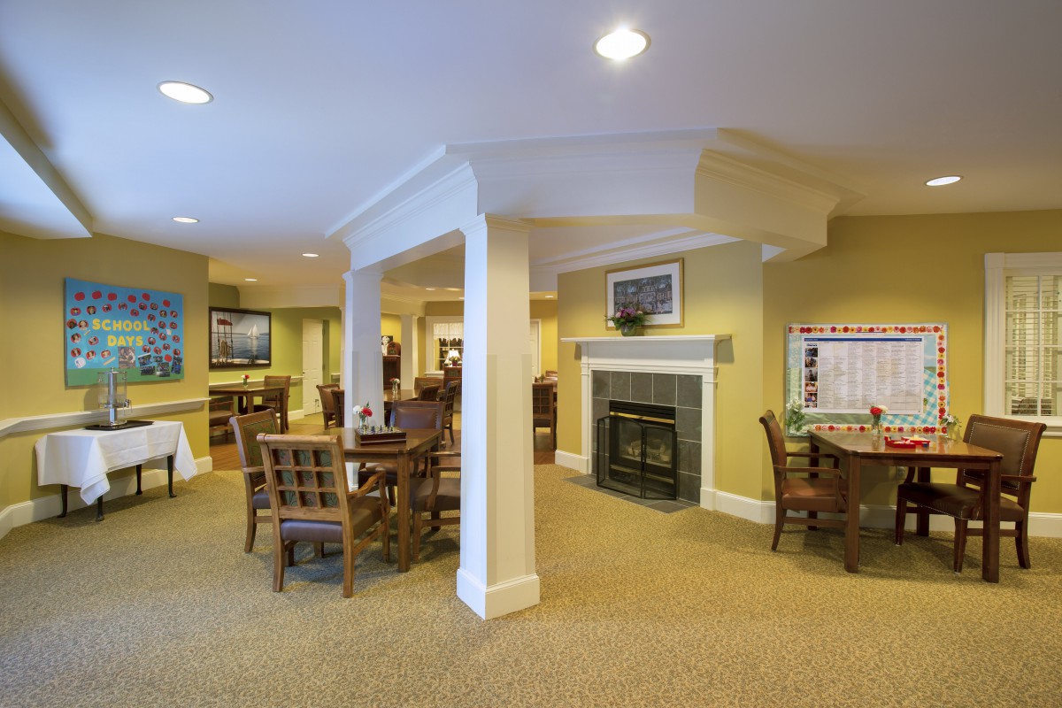 A cozy indoor space with multiple tables and chairs, featuring a fireplace and warm lighting.