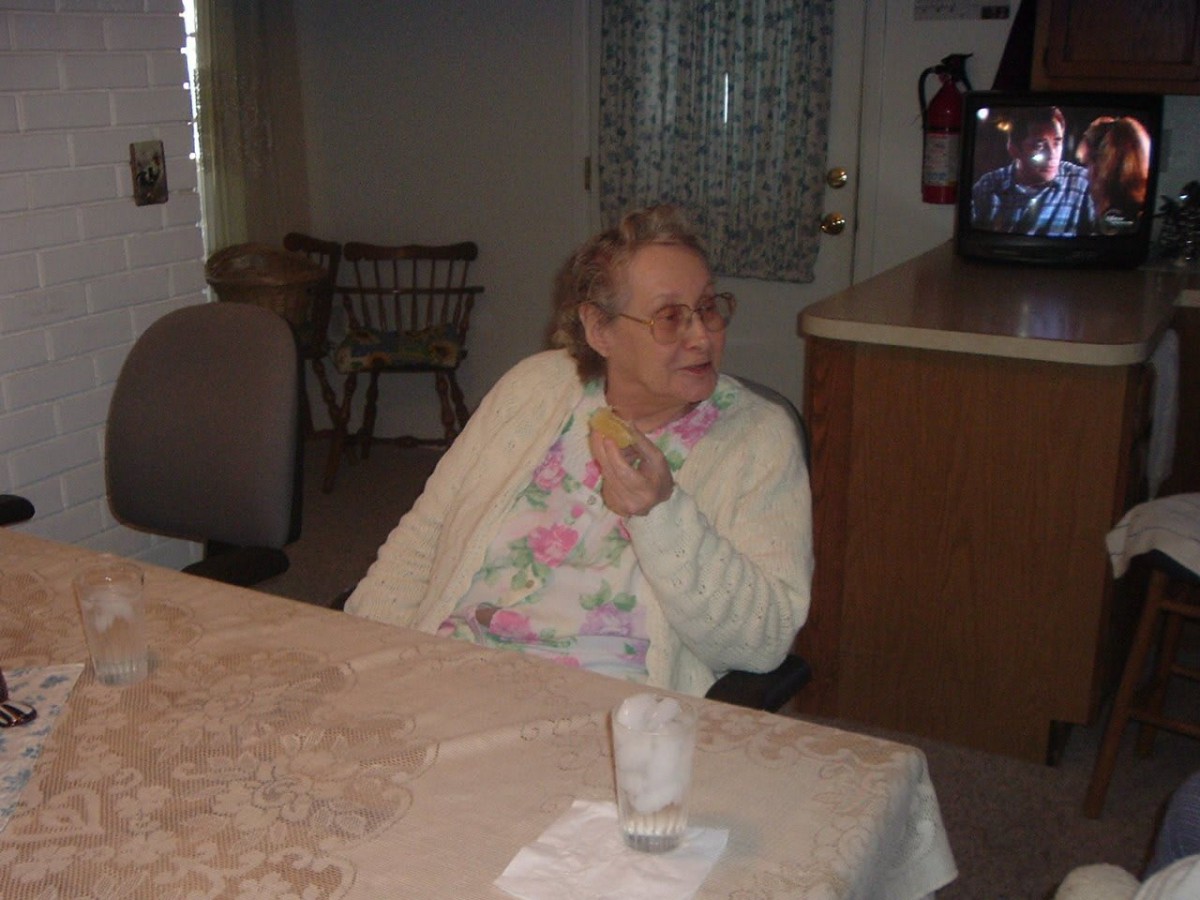 An elderly person seated at a table in a living room setting.